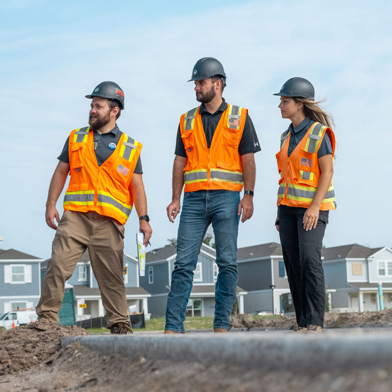 Three workers in orange vests and hard hats on site.