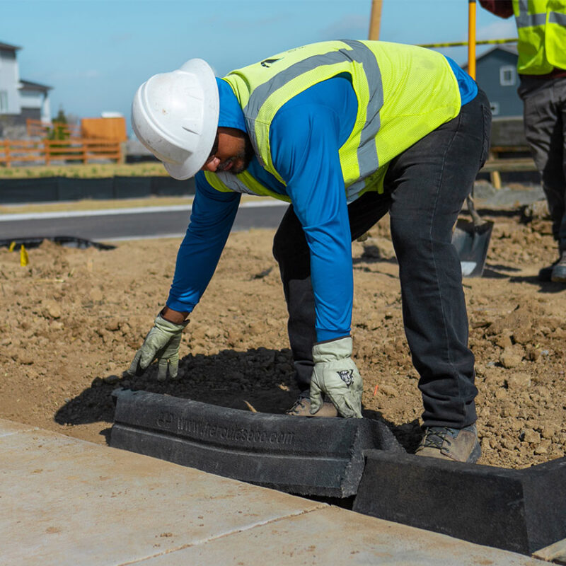 Worker in vest and helmet installs Hercules EcoBlock by sidewalk.