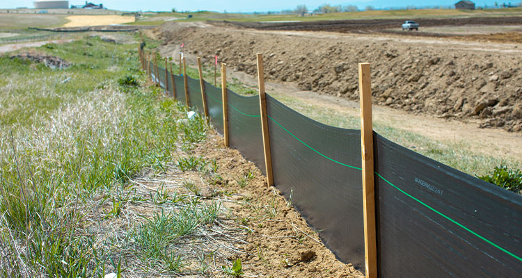 Black silt fence with wooden stakes separates soil from grass.