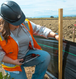 Worker in hard hat checks black silt fence with tablet.