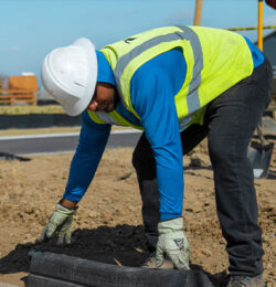 Worker in safety gear installs Hercules EcoBlock between dirt site and sidewalk.