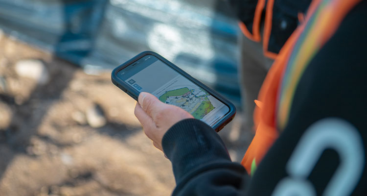 Person in safety vest holds smartphone with map at worksite.