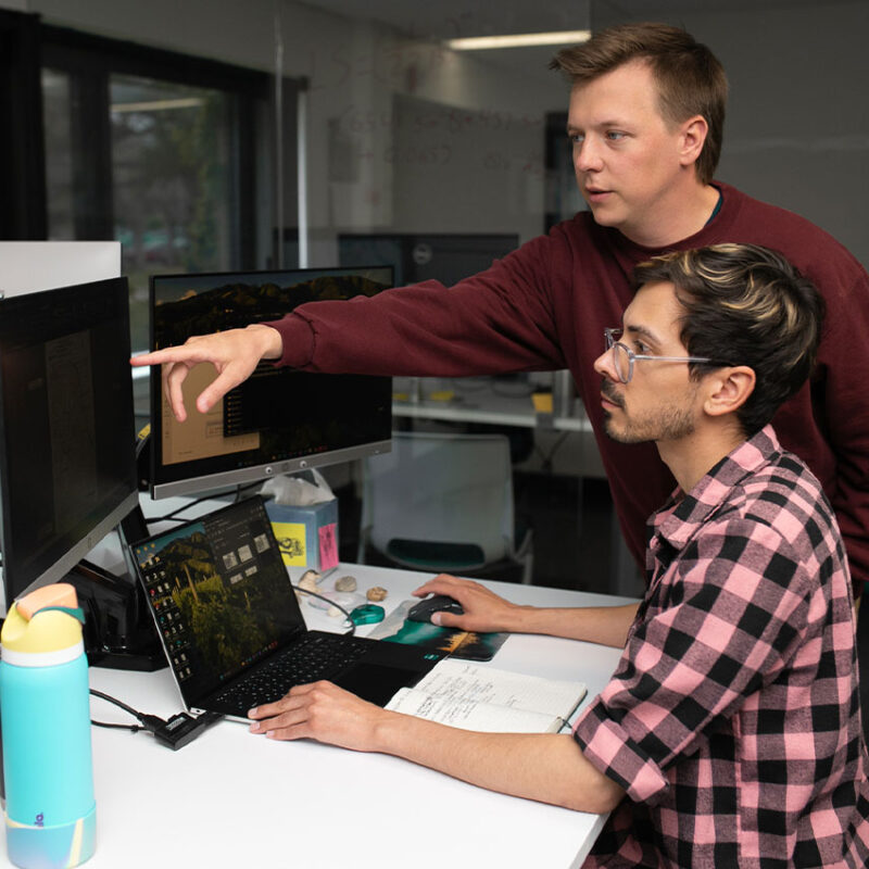 One person types while another points at a computer screen.