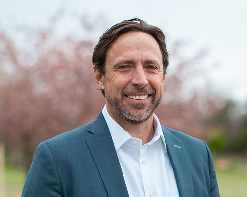 Bearded man in blue suit outdoors with blurred trees.