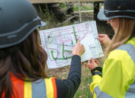 Two people in safety vests and hard hats examine a site plan.