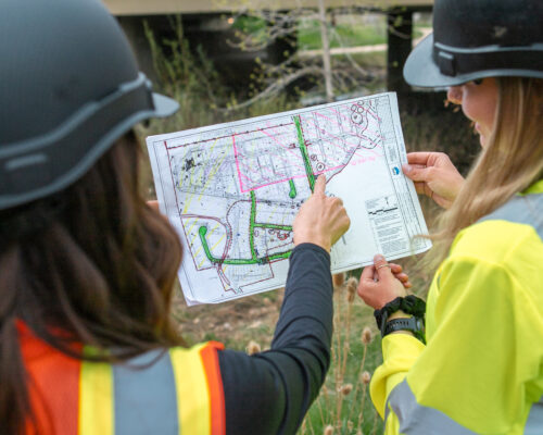 Two people in safety vests and hard hats examine a site plan.