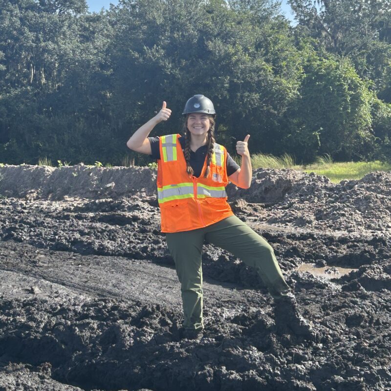 Woman smiling and thumbs-upping standing in mud
